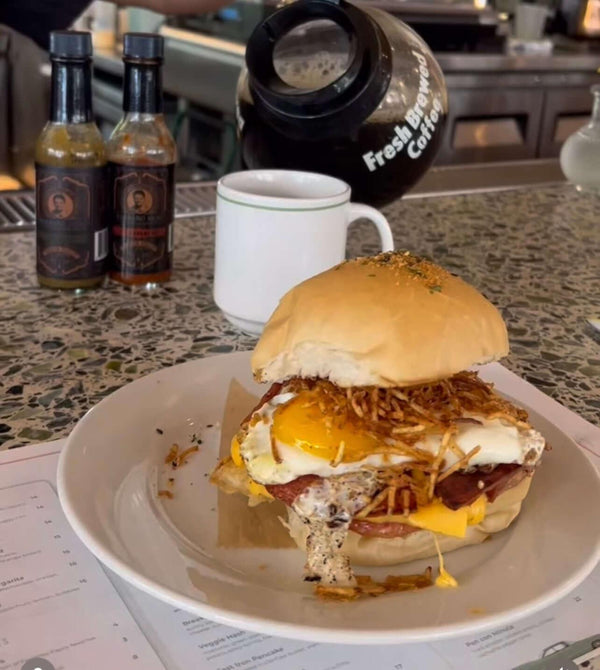Frita a caballo, a Cuban burger topped with a fried egg and shoestring potatoes on a soft bun, with Barbaro Mojo bottles on the counter behind it