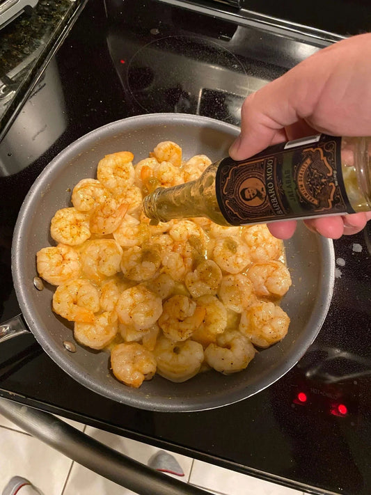 Shaking Barbaro Mojo Jalabáo hot sauce over a pan of sautéed shrimp on the stove