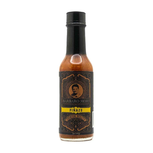 Bottle of Piñazo hot sauce, orange sauce behind a dark ornate label with a yellow name band, on a white background