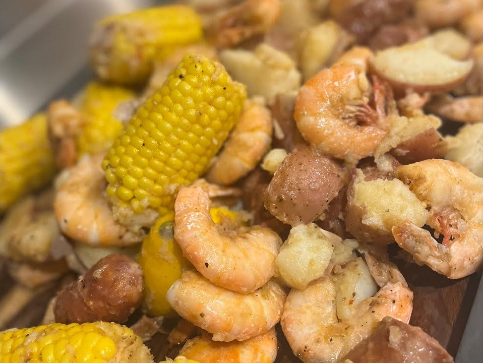 Cuban shrimp boil on a platter: shell-on peel and eat shrimp, corn on the cob, red potatoes and smoked sausage glossed with hot sauce butter