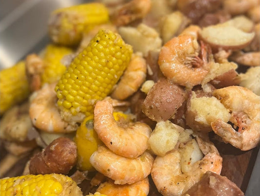 Cuban shrimp boil on a platter: shell-on peel and eat shrimp, corn on the cob, red potatoes and smoked sausage glossed with hot sauce butter
