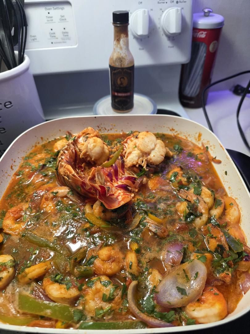 Enchilado de mariscos: shrimp, sea scallops and split Florida spiny lobster tails in a tomato sofrito with peppers, red onion and cilantro, El Havanero behind the pan