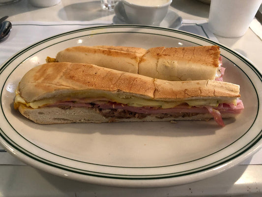 Pressed Cuban sandwich cut in half on a plate at Versailles restaurant on Calle Ocho, Miami, showing roast pork, ham, Swiss cheese and pickles