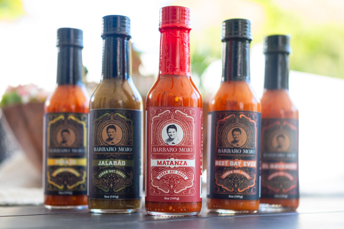 Five Barbaro Mojo Cuban hot sauce bottles with the new foil labels lined up on an outdoor table
